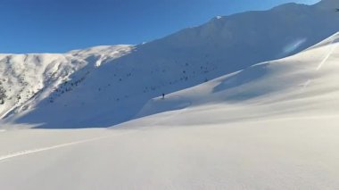 Maceraperest bir serbest kayakçı görkemli bir dağdaki el değmemiş derin toz kardan zarif bir şekilde iner ve berrak mavi gökyüzünün altında zarif izler yaratır. Bu heyecan verici pist dışı deneyim