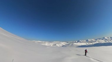 Son sınıf arkadaşları, heyecan verici bir serbest kayak turunun keyfini çıkarıyorlar. Yalnız bir kayakçı, açık mavi gökyüzünün altında, engin bir dağ manzarası boyunca taze toz karını oyar.