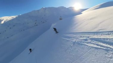 Aktif kıdemli arkadaşlar, parlak mavi gökyüzünün altında derin toz karla kaplı el değmemiş bir dağ yamacından aşağıya yeni dönüşler yaparak heyecan verici bir helikopter macerasının tadını çıkarıyorlar. Mükemmel bir kış turu.
