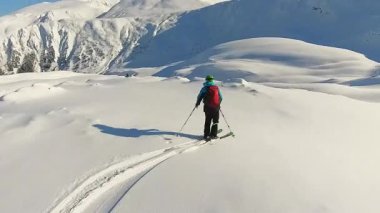 Dokunulmamış, derin toz kar üzerinde heliski yapmanın neşesini hisset. Bir serbest kayakçı temiz mavi gökyüzünün altındaki el değmemiş bir dağ yamacına zarif çizgiler çizer ve kışın tadını çıkarır.