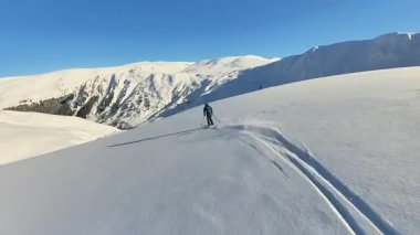 Kıdemli bir kayakçı, heyecan verici bir helezonik kayak ve serbest gezinti sırasında taze, derin toz karı oyar. Saf kış macerası sergilenen el değmemiş dağ manzarasının ve parlak mavi gökyüzünün tadını çıkar..