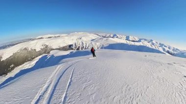Heliski 'nin coşkulu heyecanını hisset. Solo bir serbest kayakçı açık mavi gökyüzünün altında el değmemiş bir dağ arazisinde taze, derin toz karları oyuyor..