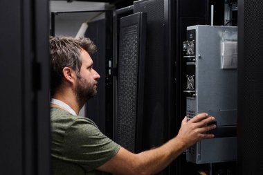 Veri merkezi teknisyeni, kontrol edilen sunucu odasındaki raflara monte edilmiş bir sunucuyu denetleyerek ağın güvenilirliğini ve donanım testini gerçekleştirir.