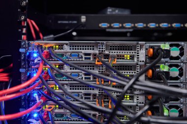 Karışık ağ kabloları, turuncu konnektörleri ve parıldayan LED durum ışıkları olan, veri merkezi altyapısı, bağlantı ve yüksek teknoloji ağ işlemleri gösteren bir sunucu rafının yakın çekimi.