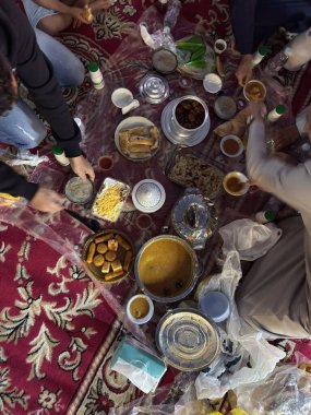 Geleneksel bir Arap ailesinin Ramazan ayında sofrada toplanıp iftarı hazırlarken ve paylaşırken çekilmiş gerçekçi bir fotoğrafı. Orijinal Ramazan atmosferi, geleneksel yemekler, kültürel