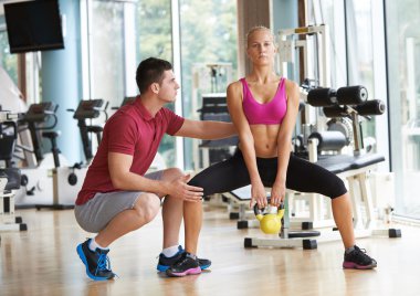 Spor salonunda spor antrenörü olan genç bir kadın ağırlık kaldırıyor.