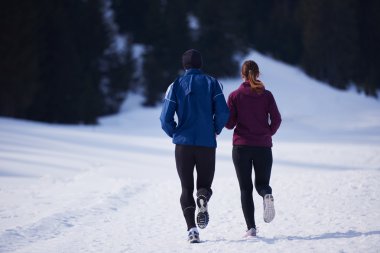 Sağlıklı genç bir çift ormanda karda koşuyor. Güzel güneşli kış gününde koşan bir sporcu.