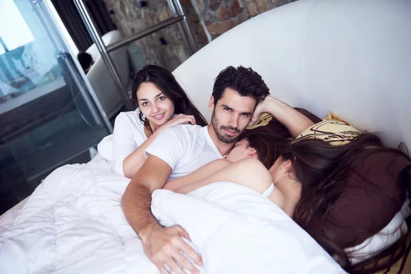 Hombre guapo en la cama con tres hermosas mujeres — Foto de Stock