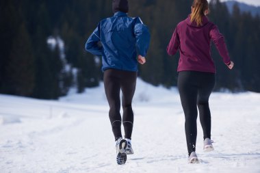 Sağlıklı genç bir çift ormanda karda koşuyor. Güzel güneşli kış gününde koşan bir sporcu.