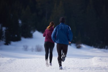 Sağlıklı genç bir çift ormanda karda koşuyor. Güzel güneşli kış gününde koşan bir sporcu.