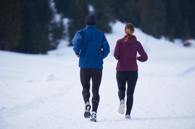 Sağlıklı genç bir çift ormanda karda koşuyor. Güzel güneşli kış gününde koşan bir sporcu.