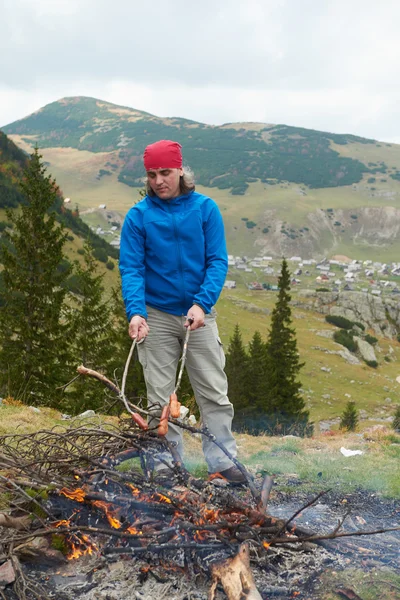 Randonnée homme préparer de savoureuses saucisses sur le feu de camp — Photo