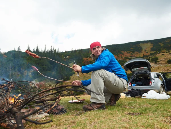 ハイキング男はキャンプファイヤーにおいしいソーセージを準備します。 — ストック写真