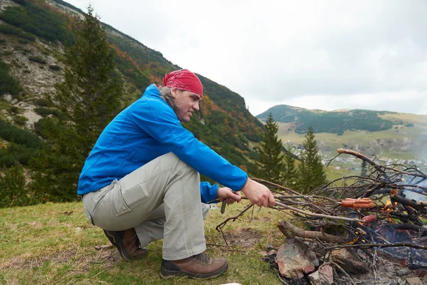 Hiking man prepare tasty sausages on campfire — Stock Photo, Image