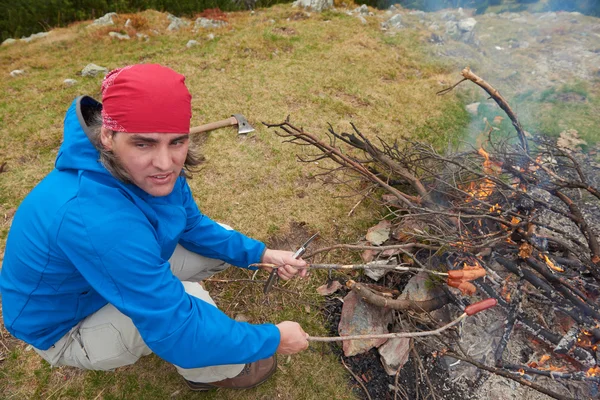 Vandring man förbereda läckra korvar på lägereld — Stockfoto