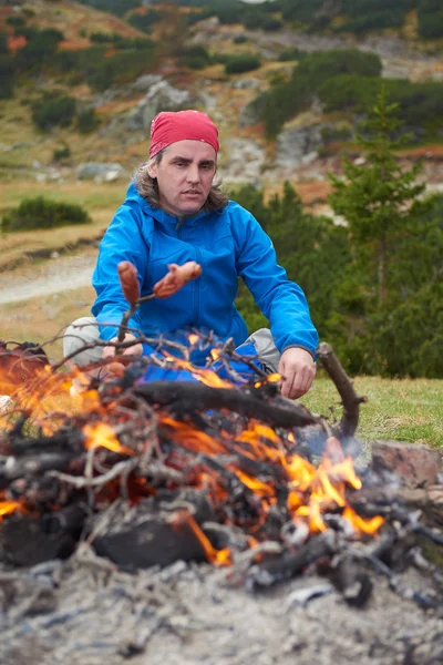 Hiking man prepare tasty sausages on campfire — Stock Photo, Image