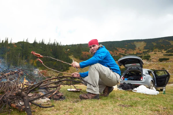 Randonnée homme préparer de savoureuses saucisses sur le feu de camp — Photo