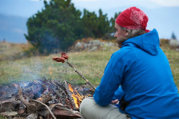 Vandring man förbereda läckra korvar på lägereld — Stockfoto