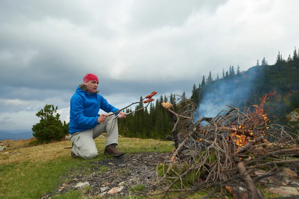 ハイキング男はキャンプファイヤーにおいしいソーセージを準備します。 — ストック写真