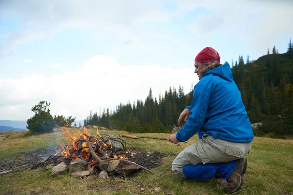 Randonnée homme préparer de savoureuses saucisses sur le feu de camp — Photo