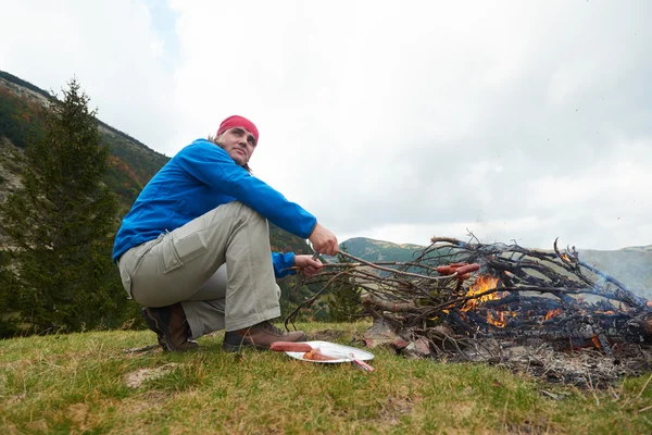 Турист готовит вкусные сосиски на костре — стоковое фото