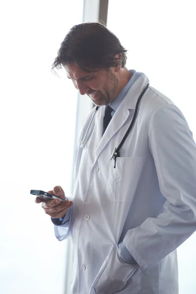 屋内で近代的な病院で彼の携帯電話でハンサムな医者 — ストック写真