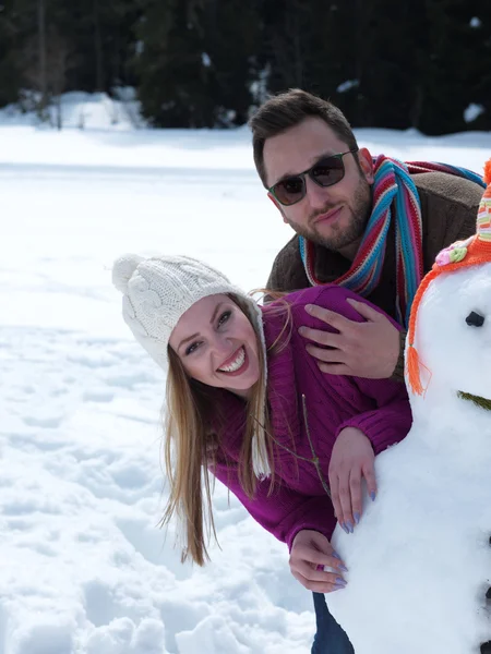Retrato de feliz pareja joven con muñeco de nieve —  Fotos de Stock