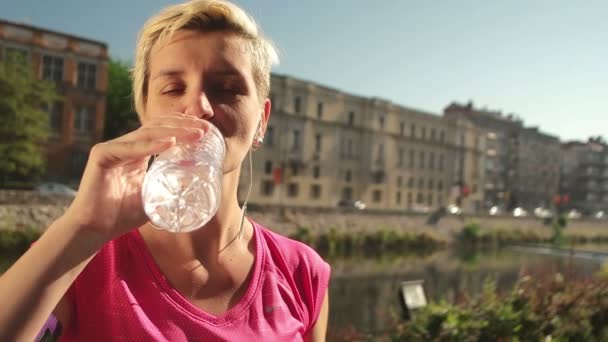 Νεαρή γυναίκα πόσιμο νερό μετά τζόκινγκ — Αρχείο Βίντεο