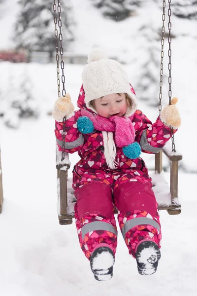 Liten flicka på snöig vinterdag swing i park — Stockfoto