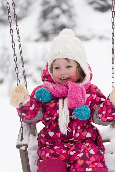 Liten flicka på snöig vinterdag swing i park — Stockfoto