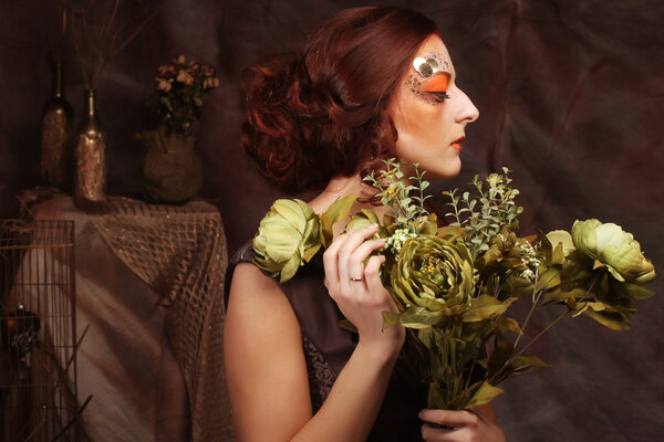Young woman with bright creative make up holding green flowers