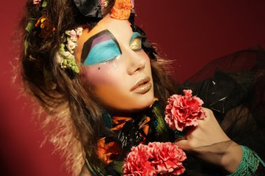 Yaratıcı makyajlı kadın pembe çiçekleri tutuyor.