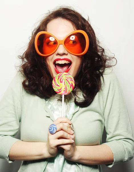 舌でロリポップを舐める大きなオレンジ色のメガネの女性 — ストック写真