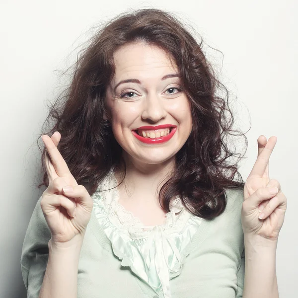 Sonriente mujer esperando duro con los dedos cruzados contra gris backg —  Fotos de Stock