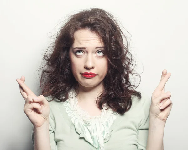 Smiley woman hoping hard with fingers crossed against gray backg — Stock Photo, Image