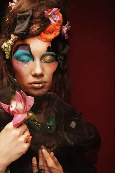 Yaratıcı makyajlı kadın pembe çiçekleri tutuyor.