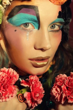 Yaratıcı makyajlı kadın pembe çiçekleri tutuyor.
