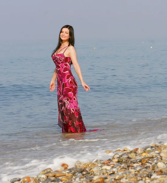 Kobieta w różowej sukience na plaży nad morzem — Zdjęcie stockowe