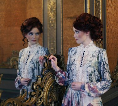 Güzel bir kadın saray odasında aynayla duruyor..