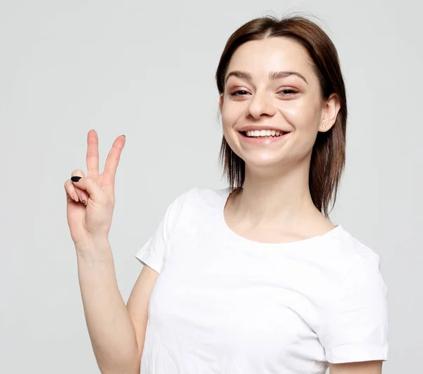 Счастливая девушка смотрит на камеру с улыбкой и показывает знак мира пальцами — стоковое фото