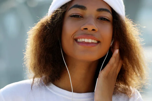 Молодая африканская американская девушка с мобильным телефоном и наушниками, улыбается, закрывается — стоковое фото