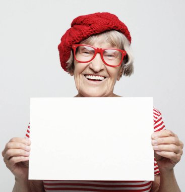 Açık gri arka planda, boş reklam panosu veya fotokopi alanı olan mutlu yaşlı kadın portresi