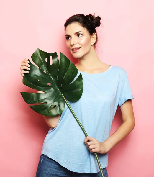 Красивая брюнетка женщина держит лист большого тропического цветка и улыбается на розовом фоне — стоковое фото
