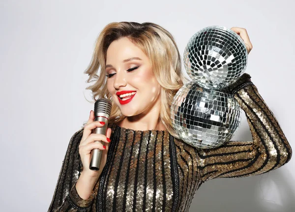 Fiatal szőke nő öltözött estélyi ruha kezében egy mikrofon és diszkó labda, ének és mosolygós — Stock Fotó