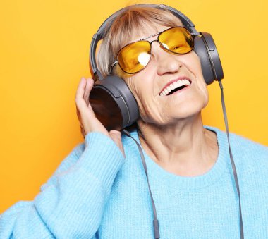 Sarı arka planda izole edilmiş akıllı telefonlu müzik dinleyen yaşlı bir kadın.