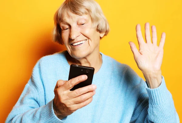Velha avó está falando com seus netos por telefone, sorrindo e cumprimentando-os. — Fotografia de Stock
