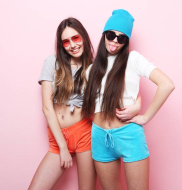 Yaşam tarzı ve insan konsepti: iki genç kız arkadaş bir arada duruyor ve eğleniyorlar. Kameraya bakıyorum. Pembe arkaplanda.