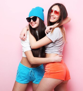 Yaşam tarzı ve insan konsepti: iki genç kız arkadaş bir arada duruyor ve eğleniyorlar. Kameraya bakıyorum. Pembe arkaplanda.