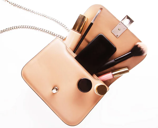 Flat lay of pink leather woman bag open out with cosmetics and smartphone over white background — Stock Photo, Image