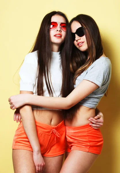 Heureux souriant jolies adolescentes portant des lunettes de soleil étreignant sur fond jaune — Photo